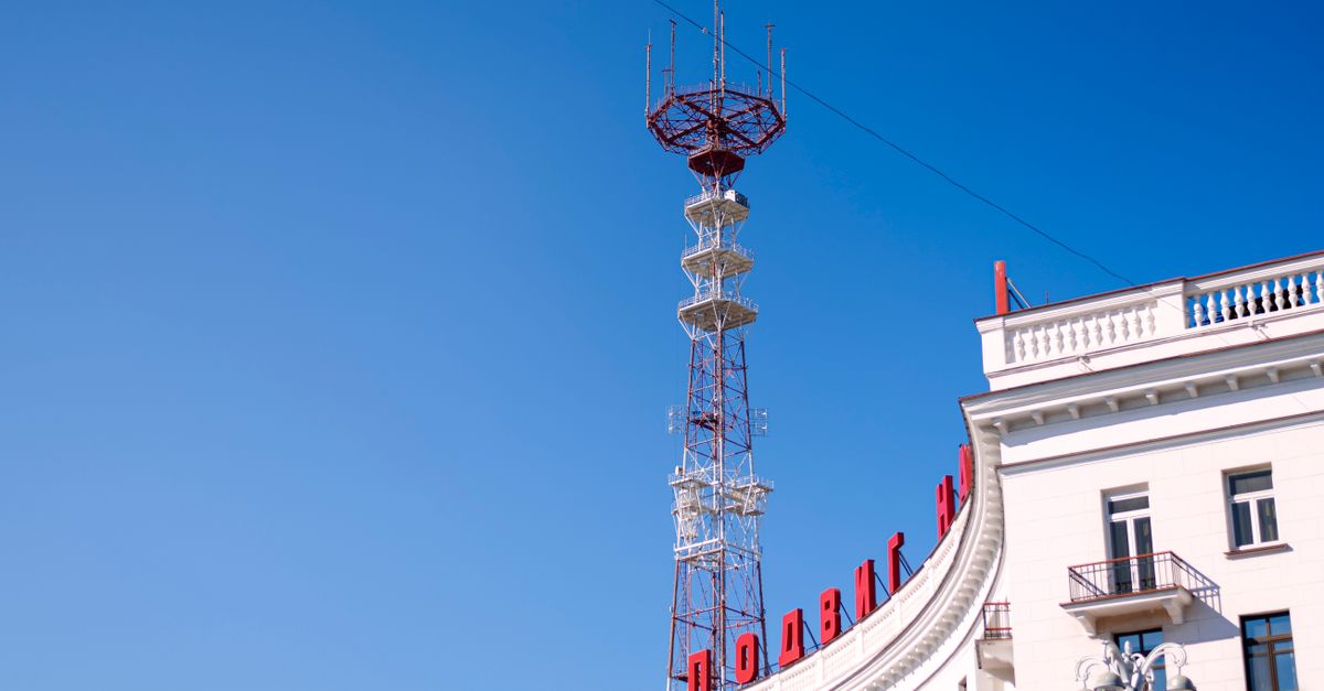 A clear view of a rooftop with a tall antenna tower against a bright blue sky, capturing urban architecture.