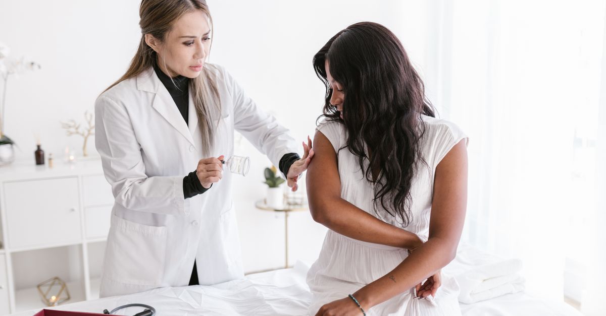 Doctor applying cupping therapy to a female patient in a white room.