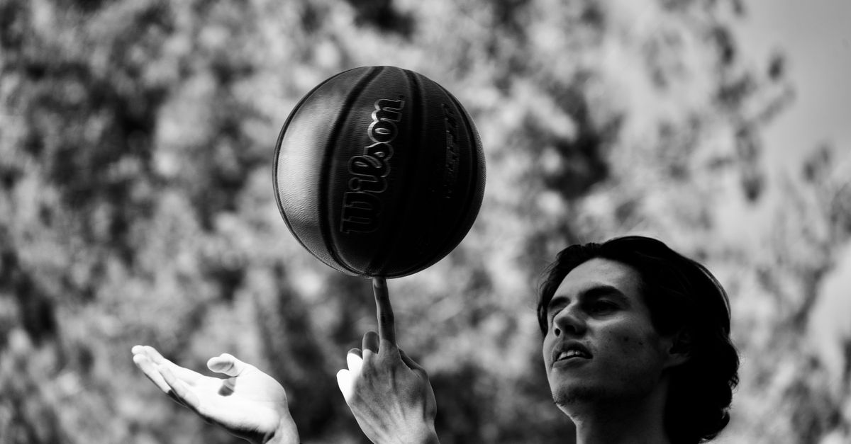 Black and white image of a basketball being spun on a finger outdoors.