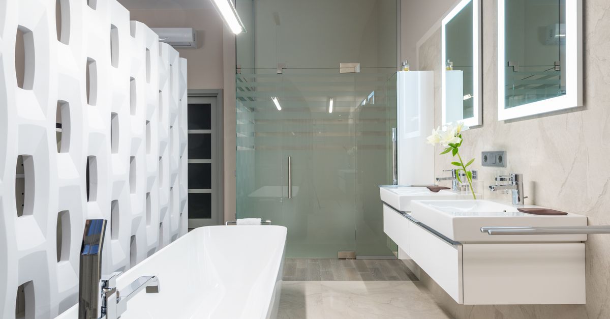 White bathtub with tap near decorative partition placed near sink and mirrors in stylish light bathroom with glass shower cabin