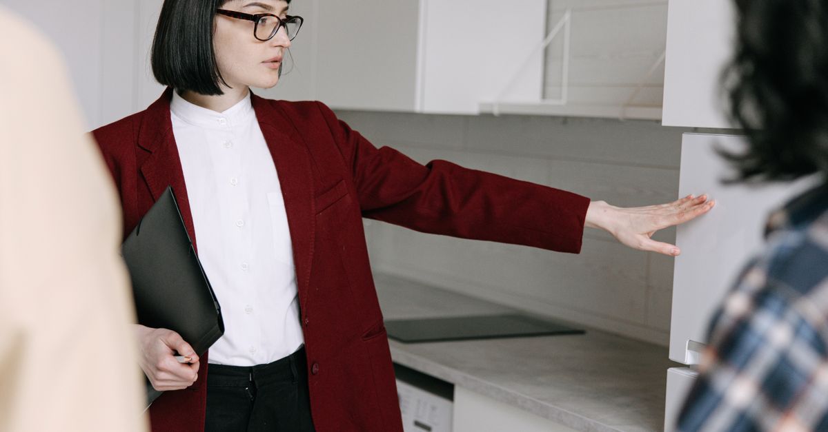 A female real estate agent demonstrates a modern kitchen to potential buyers in an apartment.