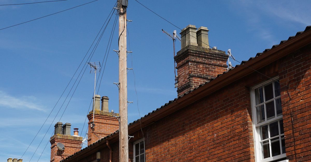 A brick building featuring chimneys and an electric post under a clear blue sky.