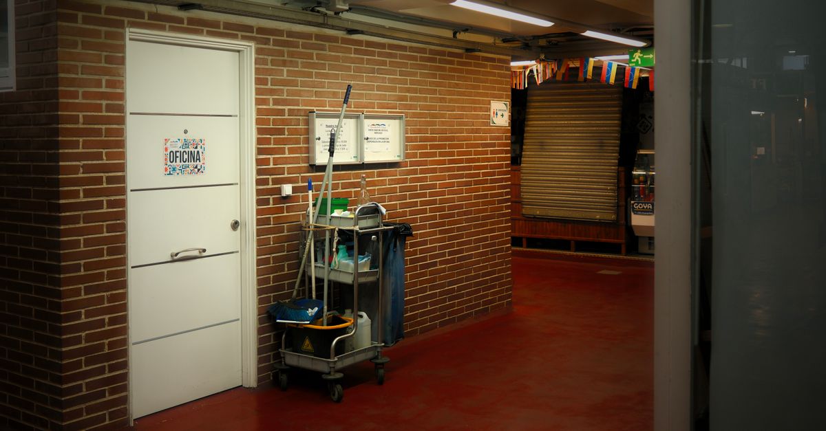 A brightly lit industrial hallway with a cleaning cart and supplies near an office door.