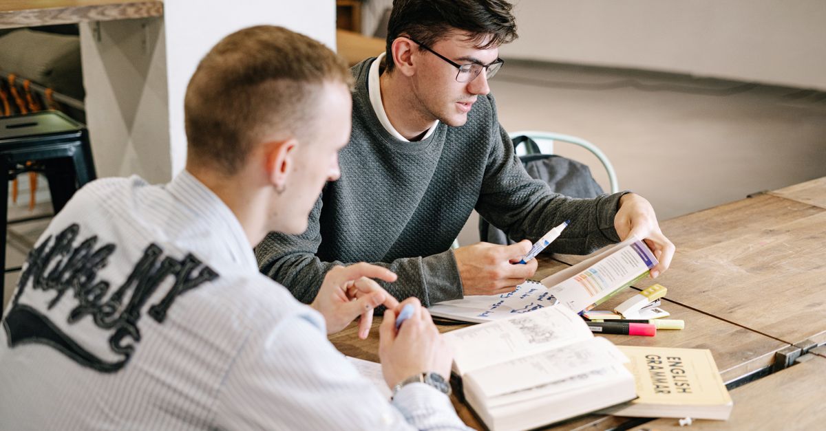 Two young men studying together, focusing on English grammar books in a modern indoor setting.