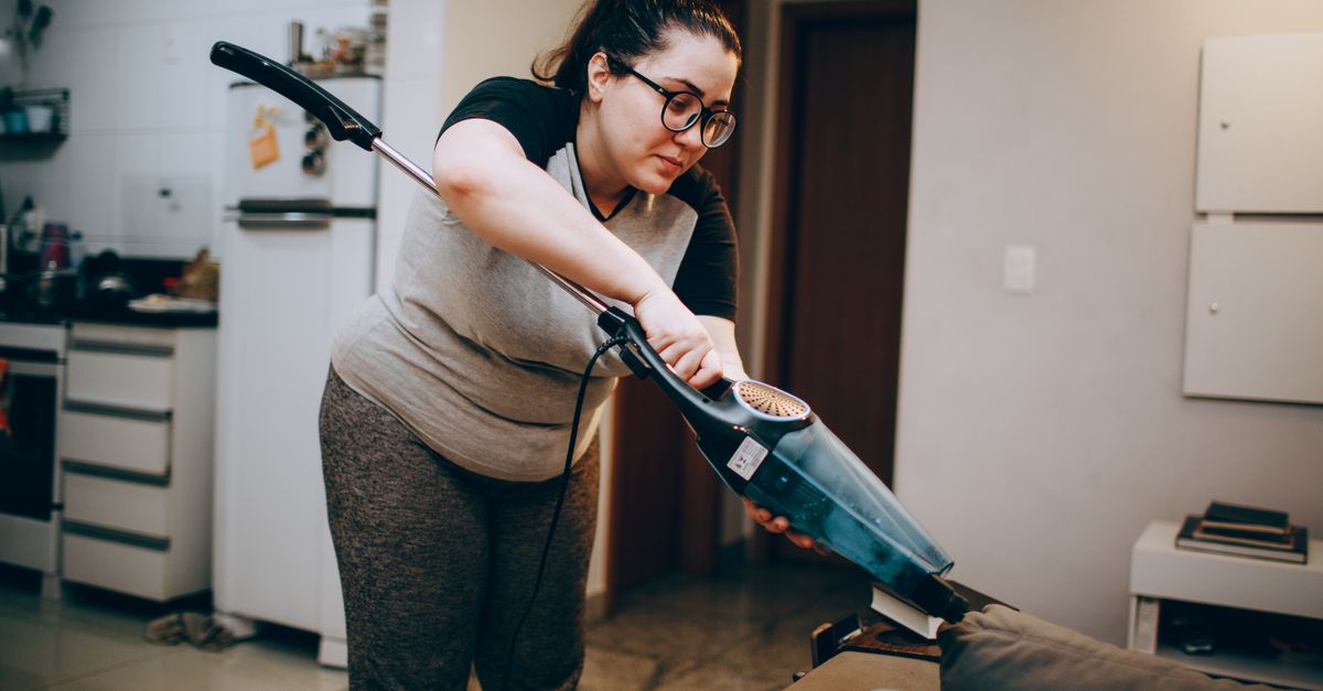 A woman vacuuming a couch in a cozy living room setting, emphasizing daily housework.