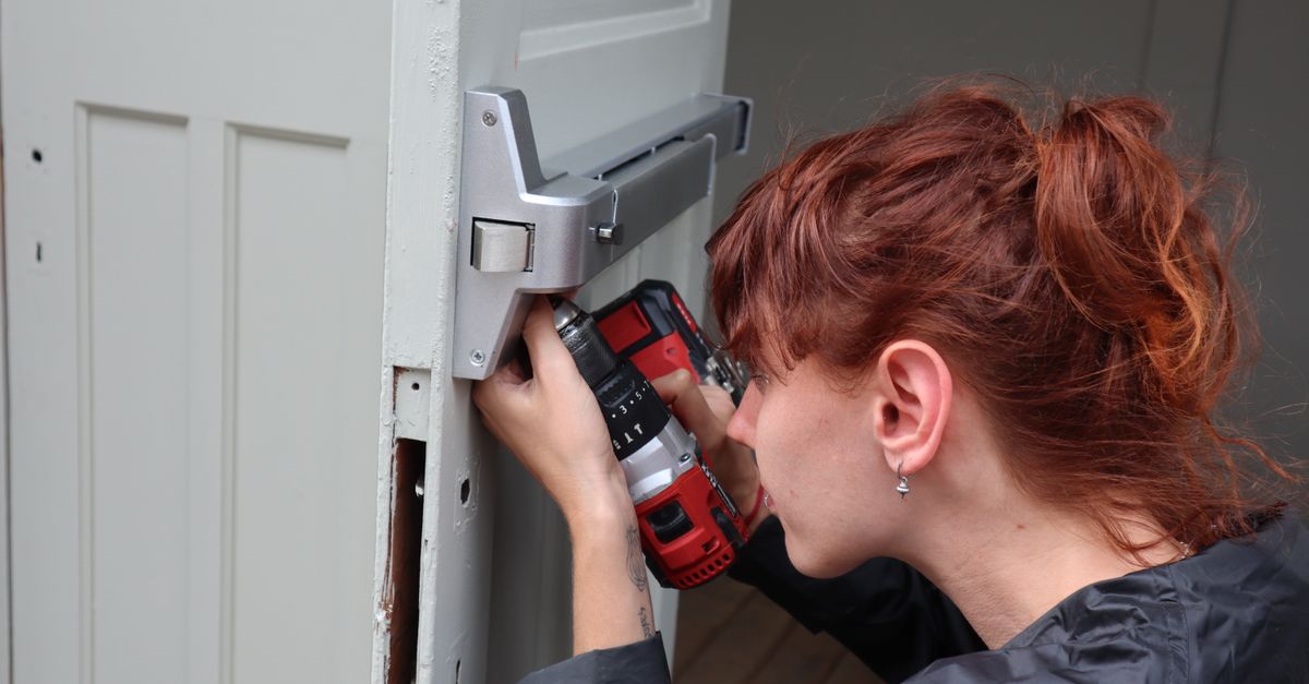 Caucasian woman focusing on door installation with power drill, side view.