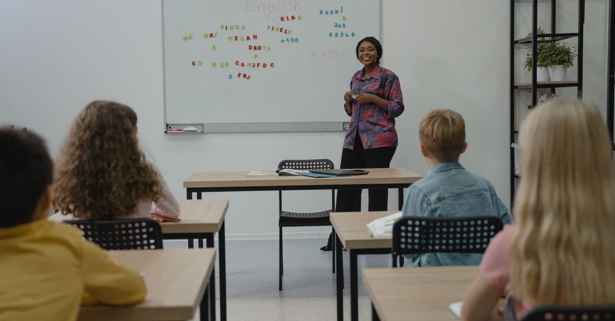 A diverse group of students in an English class with a smiling teacher at the whiteboard.