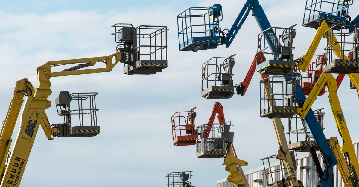 A collection of colorful boom lifts reaching toward a clear blue sky, showcasing industrial machinery.
