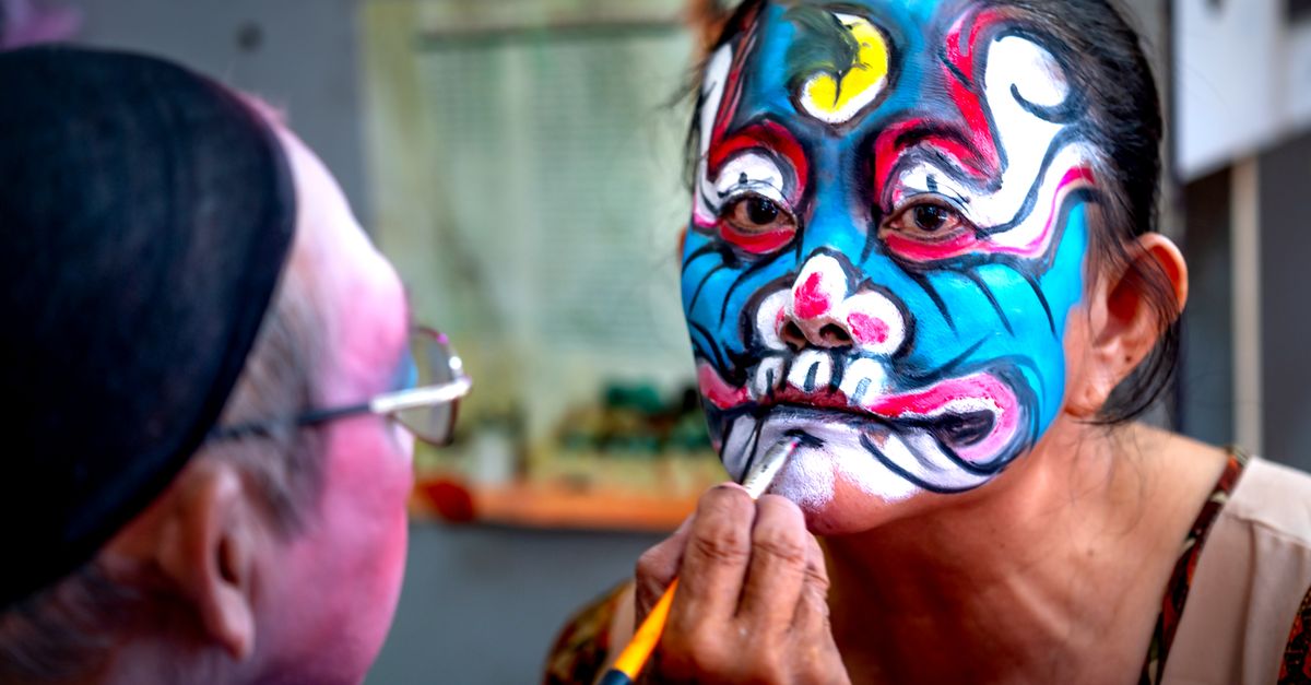 Colorful face painting in progress at a lively cultural festival indoors.