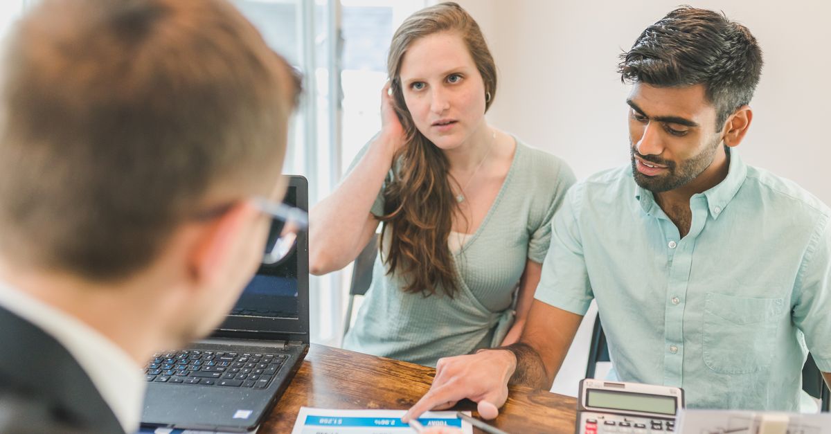 A young couple consults with a realtor about buying a home, indoors in a modern office setting.