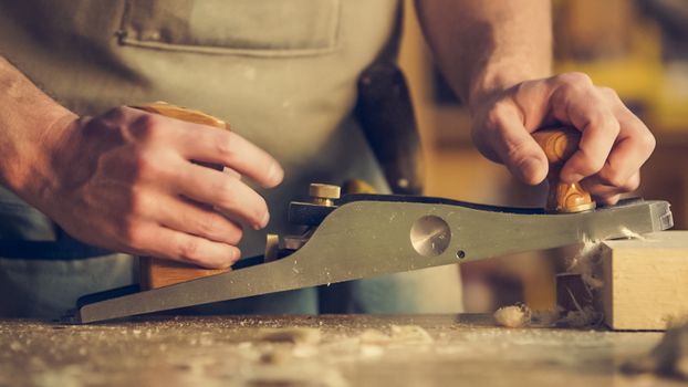 A carpenter skillfully using a hand plane on a wooden surface indoors.