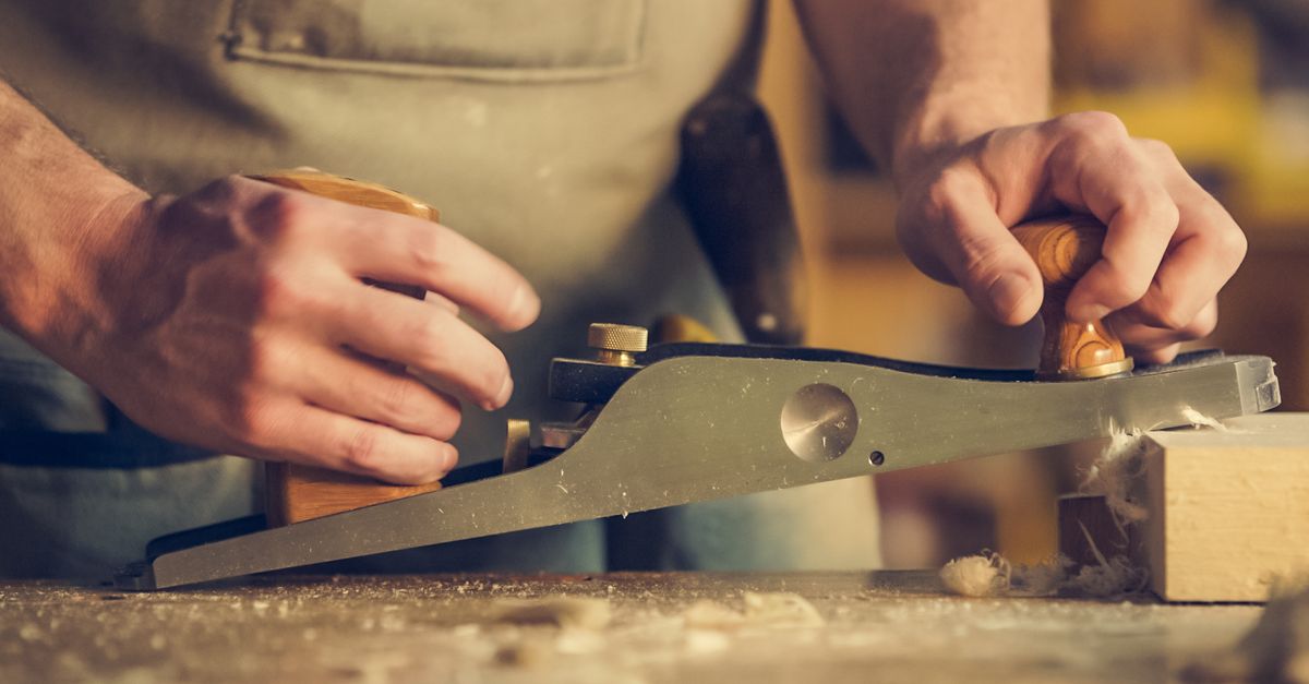 A carpenter skillfully using a hand plane on a wooden surface indoors.