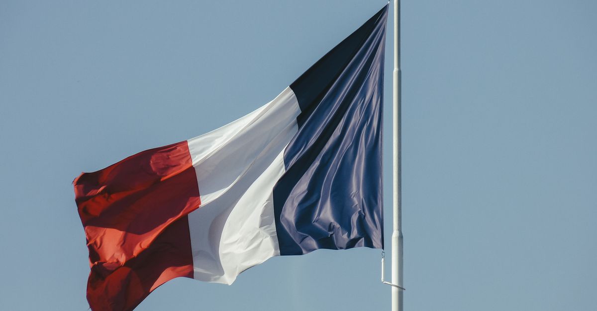 Colorful french flag on pole waving in air against blue sky on sunny weather on celebration day in summer outside