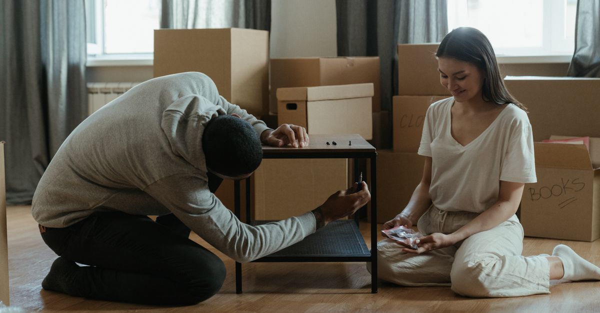 A couple assembling a coffee table amid stacked moving boxes in their new home.