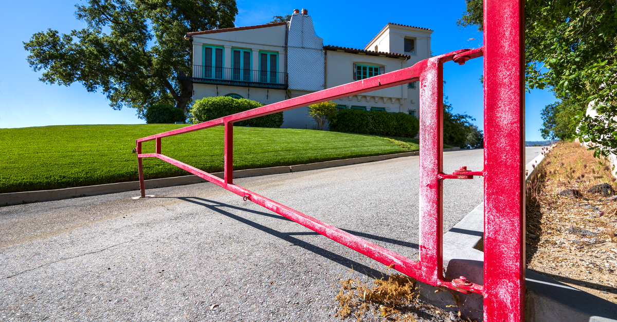 A bold red gate on a sunny day, marking the entrance to a beautiful hillside residence.