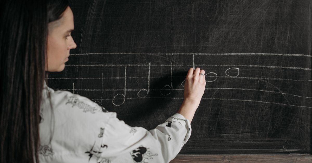 A woman writing music notation on a blackboard during a lesson.