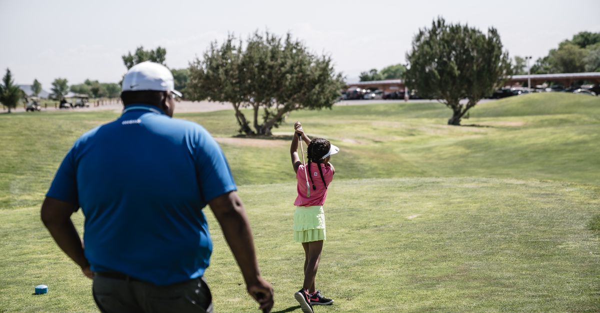 A young girl practices her golf swing under the guidance of her father on a sunny day at the golf course.
