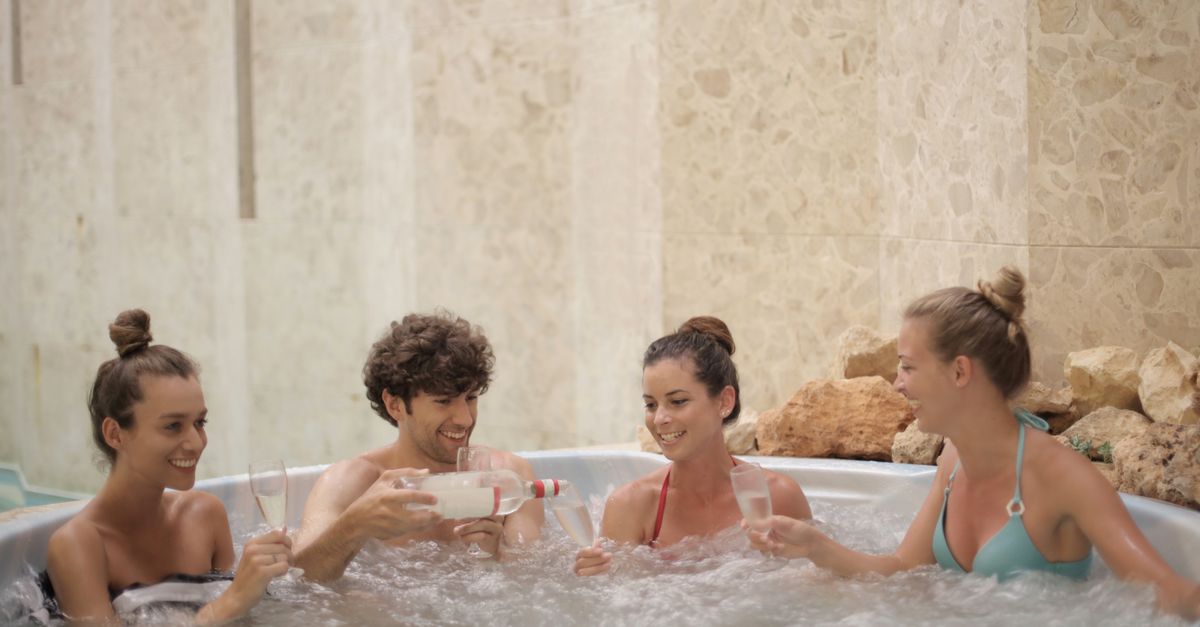 Friends having fun and relaxing together in a jacuzzi with drinks indoors.
