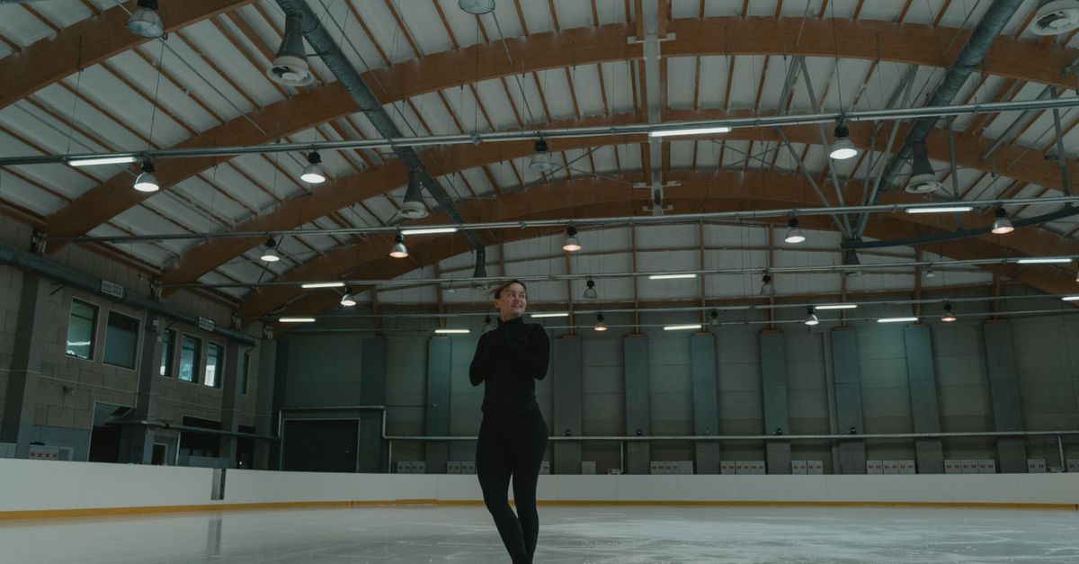 A figure skater gracefully performs on an indoor ice rink, showcasing skill and elegance.