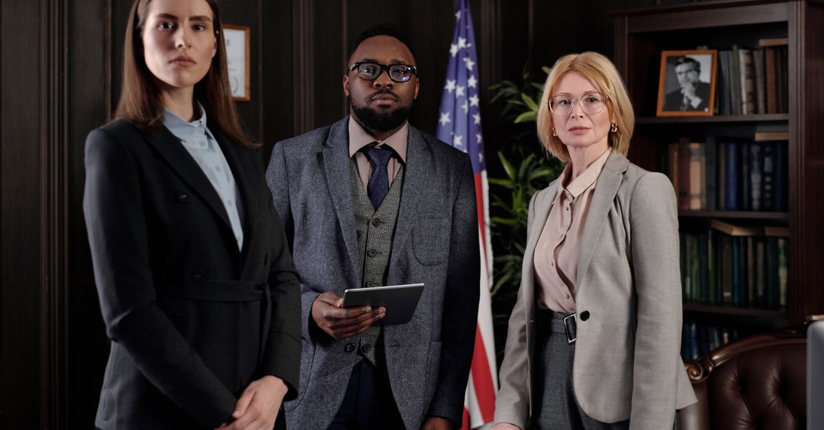 A diverse group of professionals in a formal office setting featuring an American flag and bookshelves.