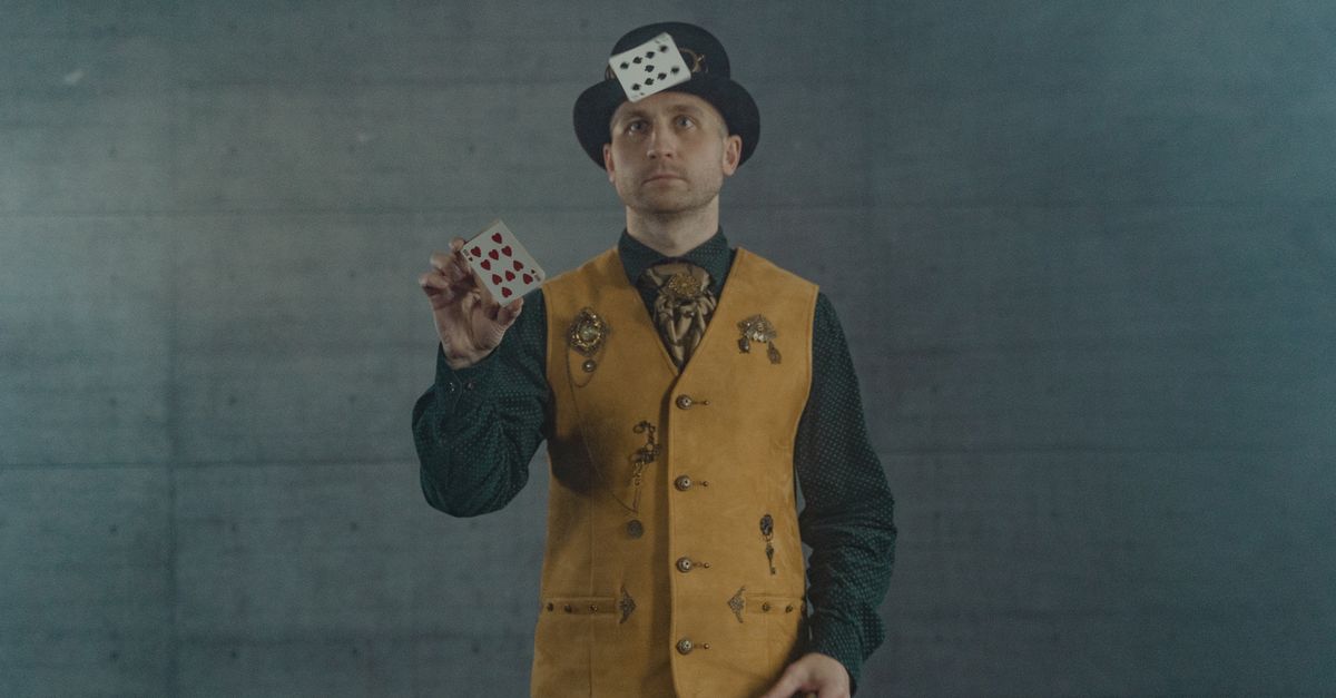 A magician in a brown vest performing a card trick indoors, showcasing skill and magic.