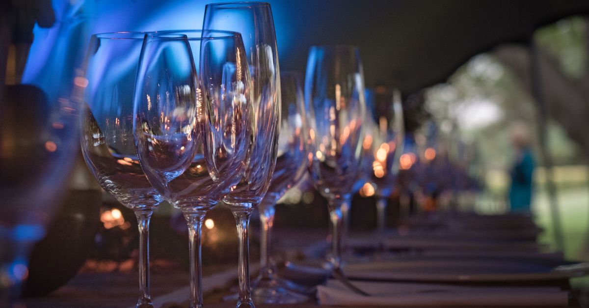 A row of sparkling crystal glasses on a dimly lit event table setting.