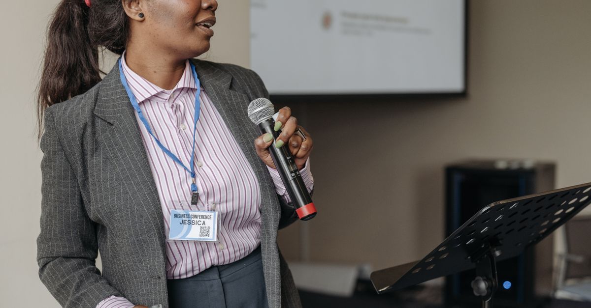 Woman in professional attire presenting at a business seminar with microphone.