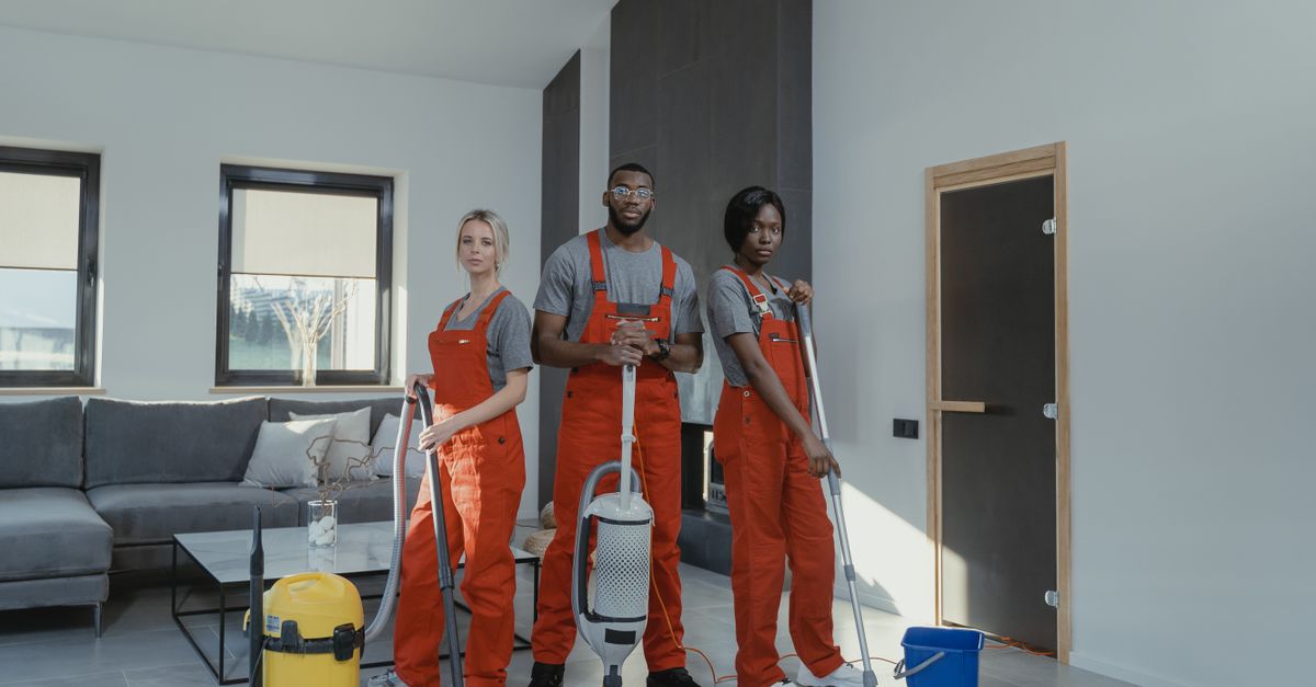 Diverse cleaning team in red uniforms ready to sanitize a modern living room with vacuum and mop.