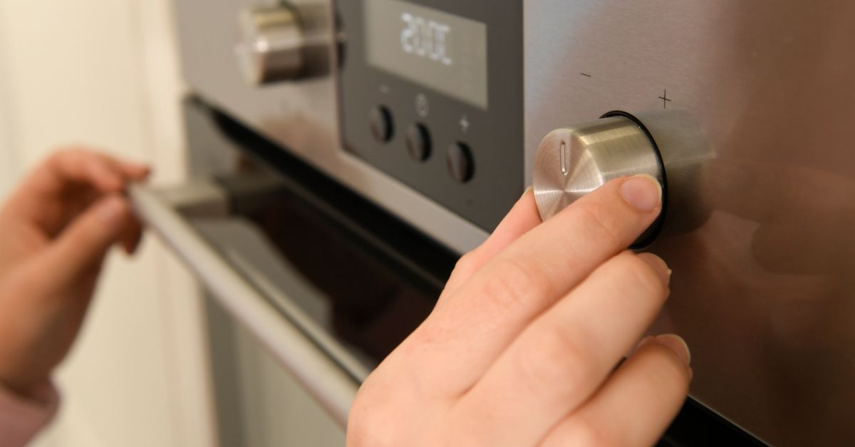 Close-up of hands adjusting the temperature dial on a modern kitchen oven.