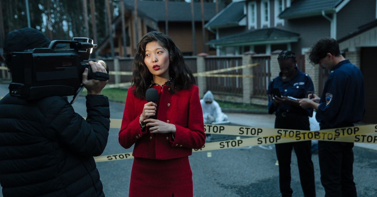 A journalist reporting from a crime scene with police officers and cameraman.