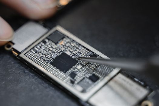 Detailed view of a technician using tweezers to fix an electronic circuit board.