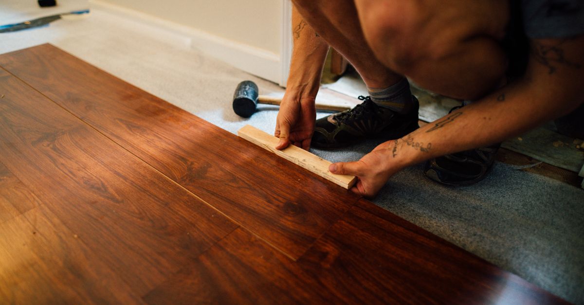 Faceless male master laying wooden laminate flooring using mallet in apartment during renovation