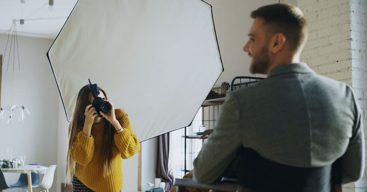 A professional photographer captures a portrait indoors using softbox lighting for a client photoshoot.