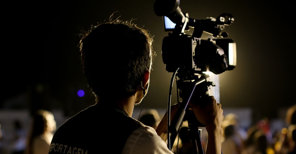 A cameraman filming an event outdoors at night with professional equipment, capturing the vibrant atmosphere.