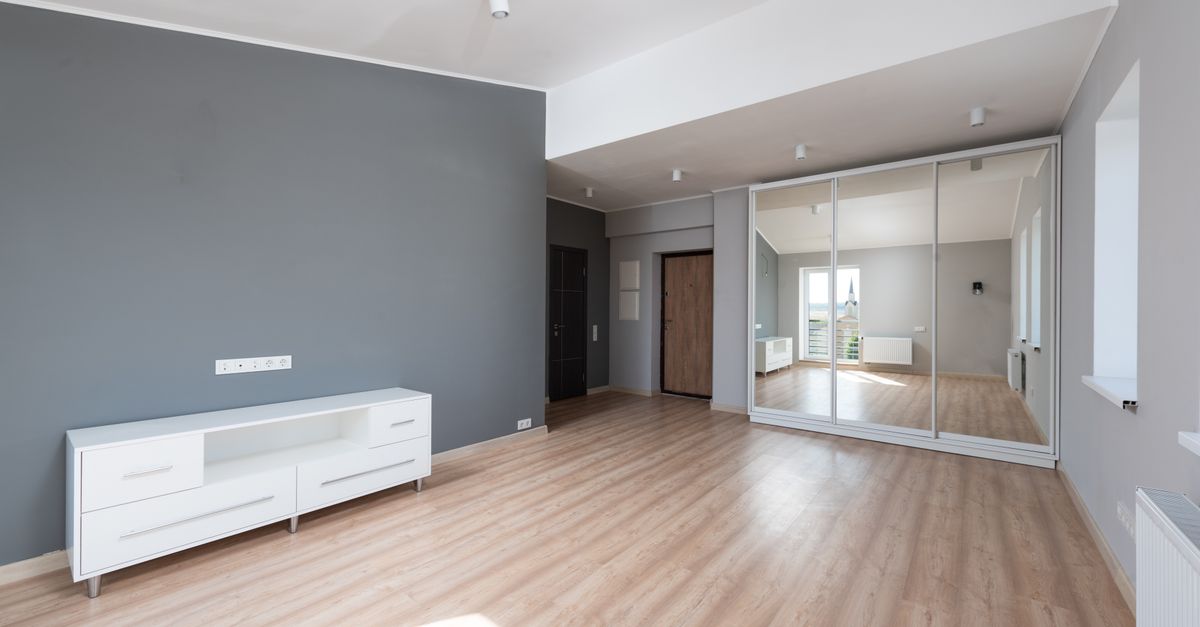 Spacious empty room with wooden flooring and minimalist style furniture.
