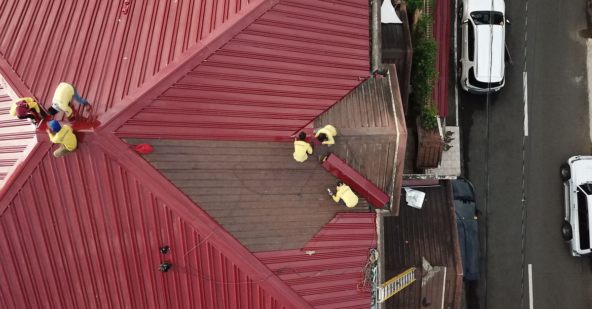 Aerial view of workers repairing a red metal roof in Quezon City, Philippines.