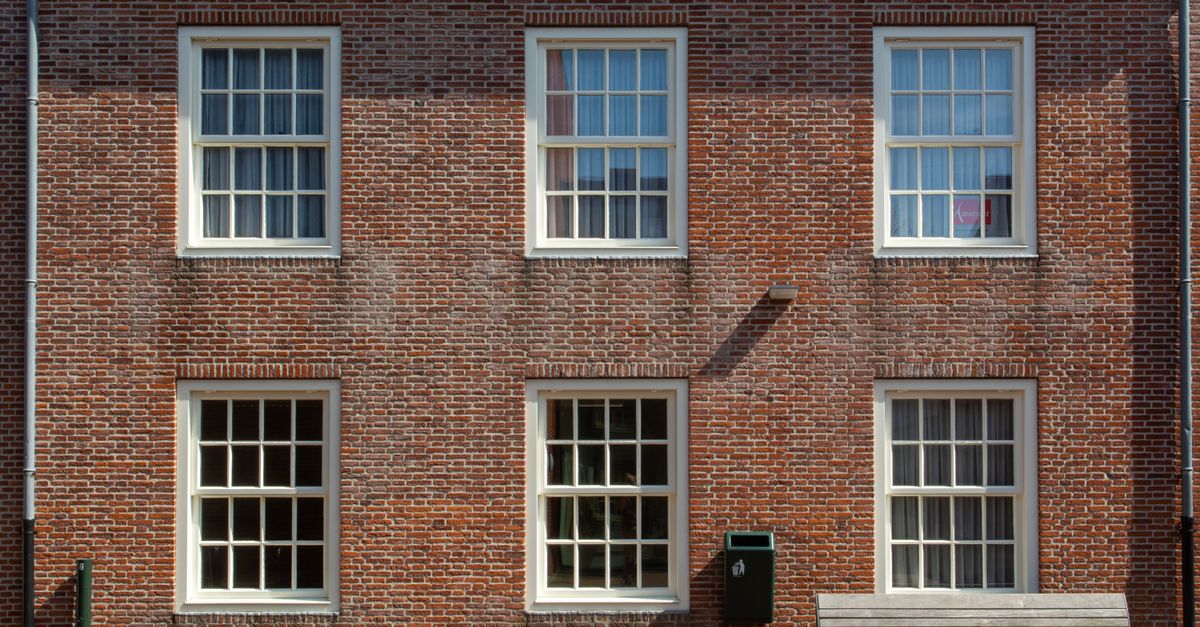 Front view of a brick building facade with sash windows and a wooden bench.