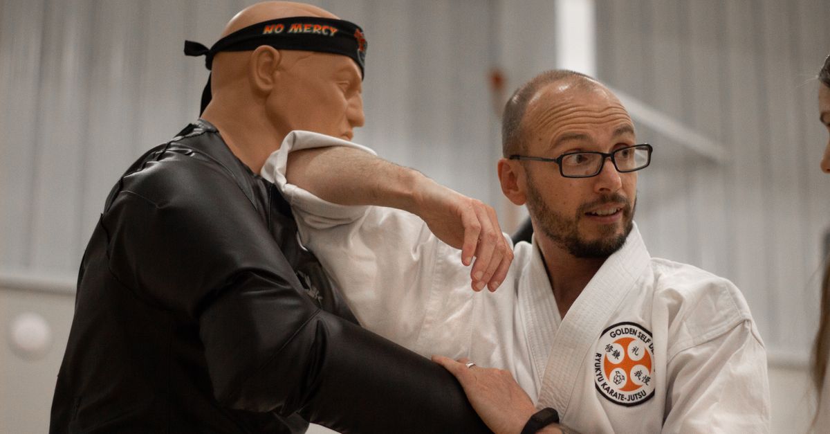 An instructor teaches self-defense using a martial arts dummy indoors.