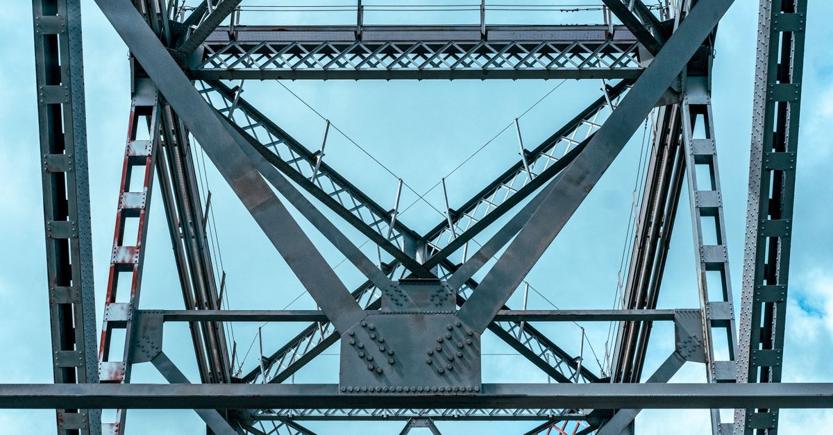 Close-up view of a steel bridge's intricate metal design towering against a clear blue sky.