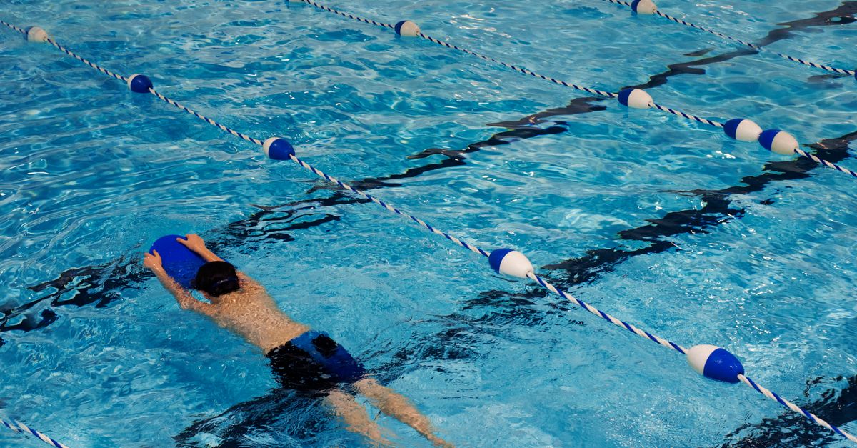 A young swimmer practicing with a kickboard in a swimming pool on a sunny day.