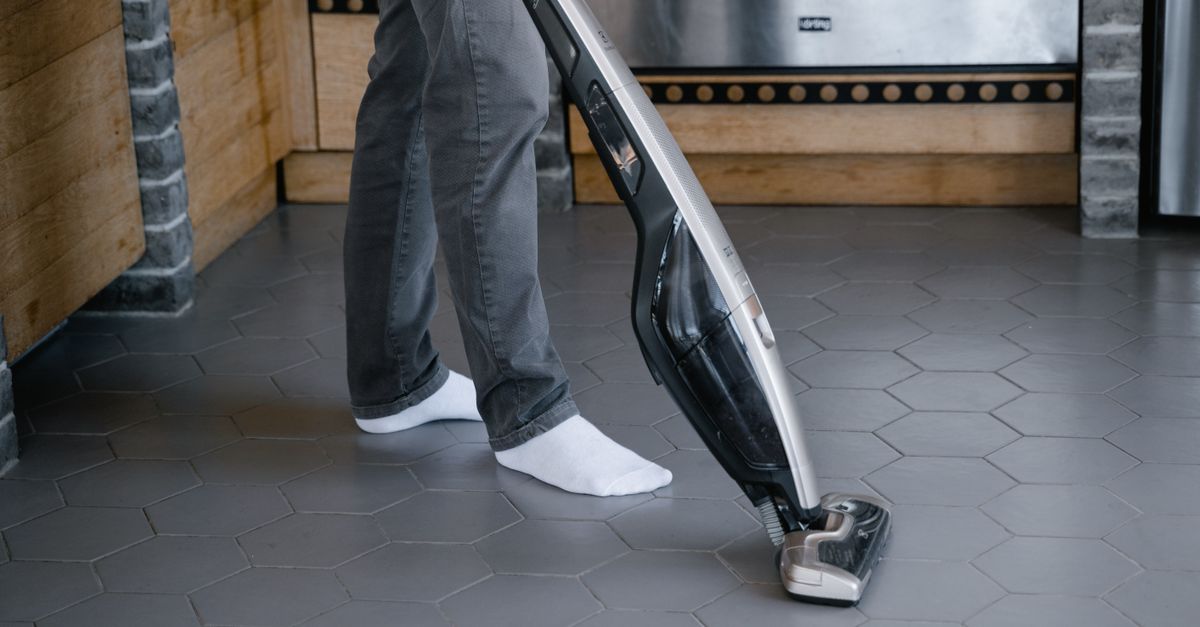 A person cleaning a tiled floor with a modern vacuum cleaner indoors.