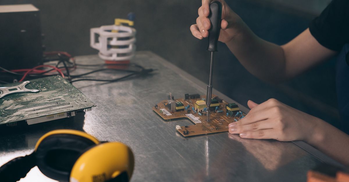 Close-up of hands working on electronic circuit board in workshop.