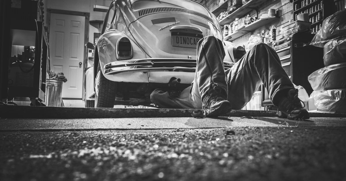 Mechanic working beneath a classic Volkswagen Beetle in a vintage garage setting.