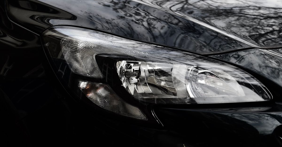 Polished reflecting surface of black modern car hood with glossy headlight on street