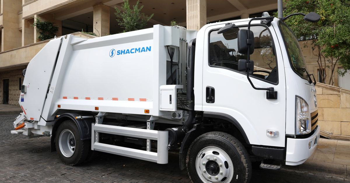 White Shacman garbage truck parked on a cobblestone street in an urban area, ready for waste collection.