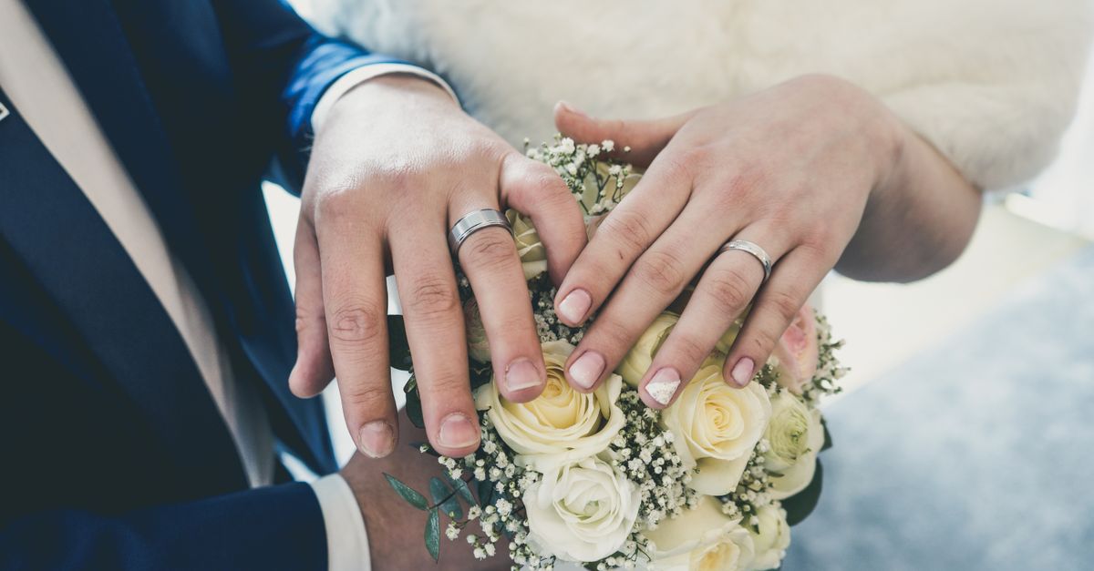 Intimate close-up of a newlywed couple's hands showcasing wedding rings with a white rose bouquet.