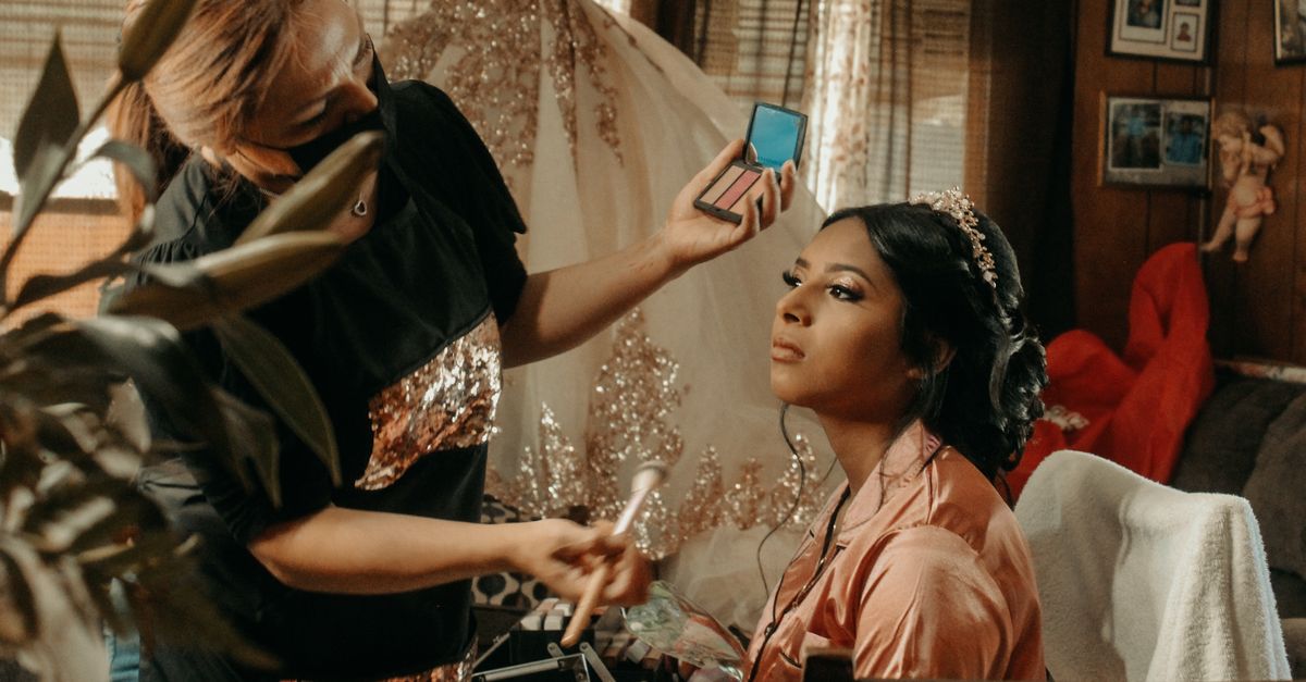A makeup artist applies cosmetics to a bride during wedding preparations indoors.