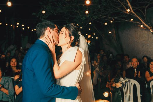 Newlywed couple sharing a romantic kiss under enchanting outdoor string lights.