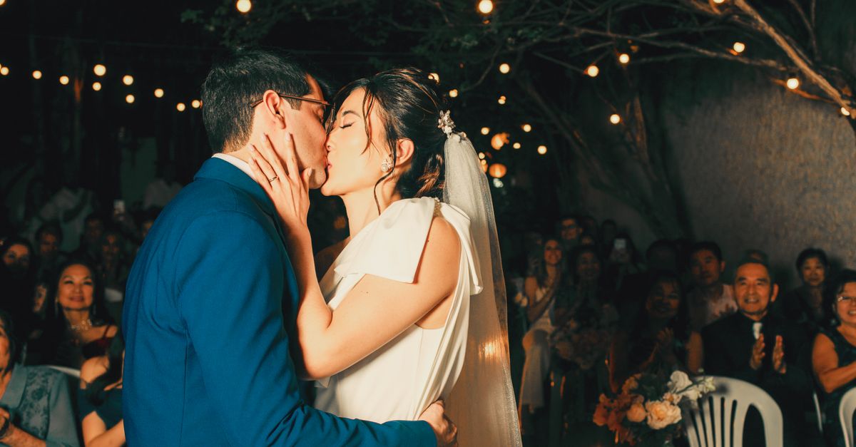 Newlywed couple sharing a romantic kiss under enchanting outdoor string lights.