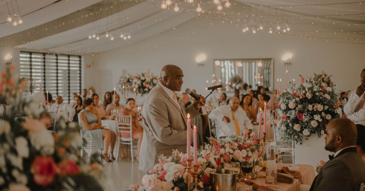 Beautiful indoor wedding reception with floral arrangements and guests enjoying a speech.
